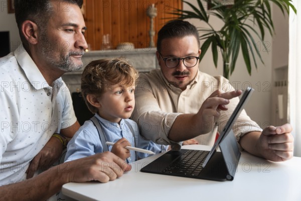 A loving gay couple enjoys quality time with their young son while using a tablet. The family is