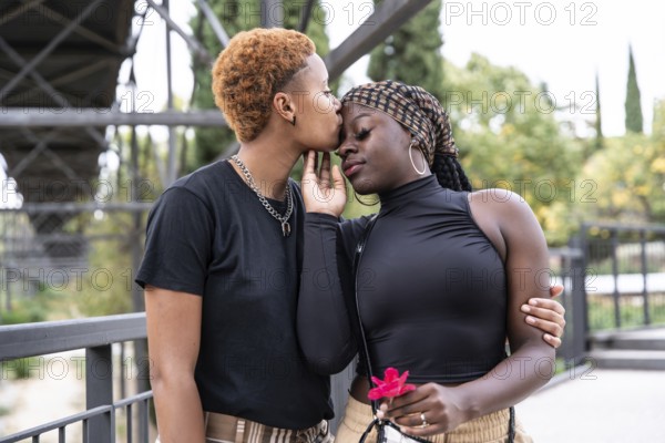 A loving LGBTQ multiethnic couple embraces in a park, sharing a tender moment. One partner gently