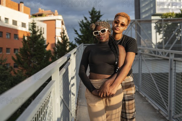 A loving LGBT multiethnic couple embraces warmly on a sunny urban bridge. They share a joyful and