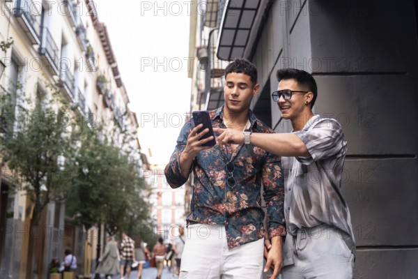 A joyful latin gay couple using a smartphone while strolling through a vibrant street in Madrid,