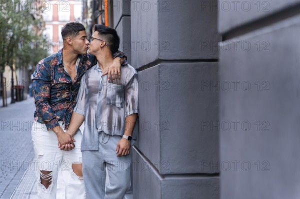 A latin gay couple shares a tender kiss while holding hands in the vibrant streets of Madrid. The