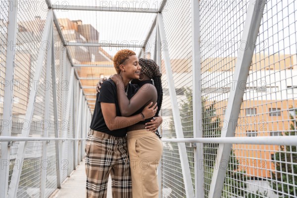 A joyful LGBT multiethnic couple shares a warm embrace on a metal walkway bridge, surrounded by
