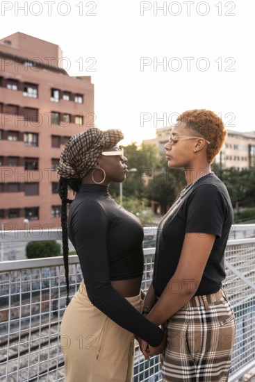 A loving LGBT multiethnic couple stands closely, facing each other, on an outdoor walkway. The