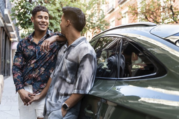 A joyful latin gay couple shares a moment by a car on a charming street in Madrid, showcasing the