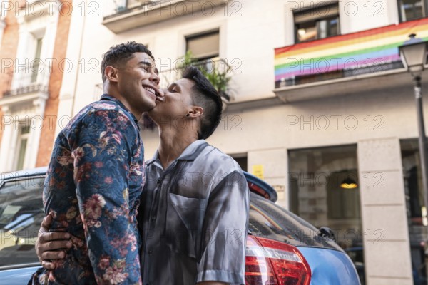 A joyful latin gay couple shares a tender moment on a lively street in Madrid, with a rainbow flag