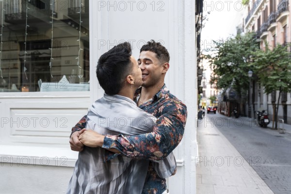 A joyful latin gay couple embraces and shares a tender moment on a charming street in Madrid. The
