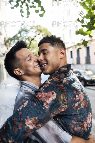 A joyful latin gay couple embraces lovingly on a sunny street in Madrid. The background features