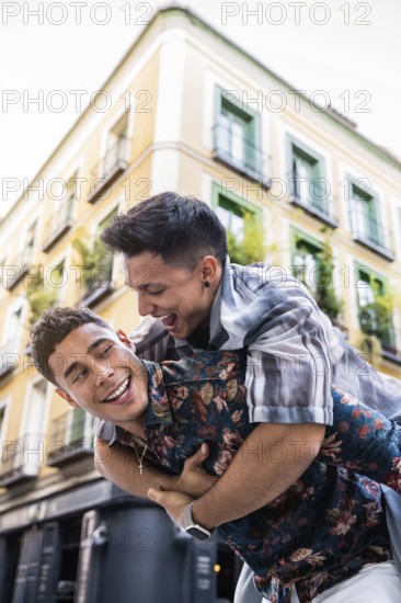 A joyful latin gay couple share a playful piggyback ride in the vibrant streets of Madrid. The warm