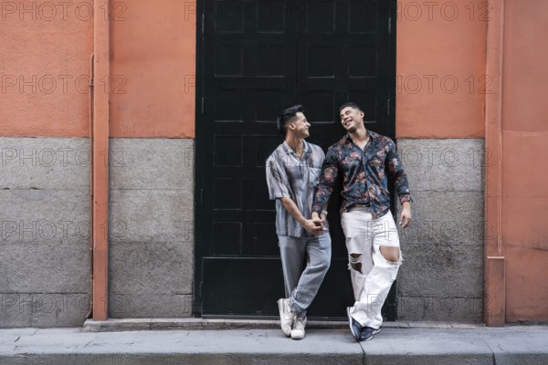 A joyful latin gay couple shares a tender moment holding hands, standing in front of a colorful