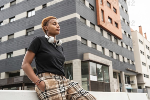 A confident young hispanic transgender with short hair wearing headphones and plaid pants, leaning