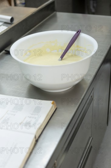 A mixing bowl with batter and a purple spatula on a stainless steel counter, next to an open recipe