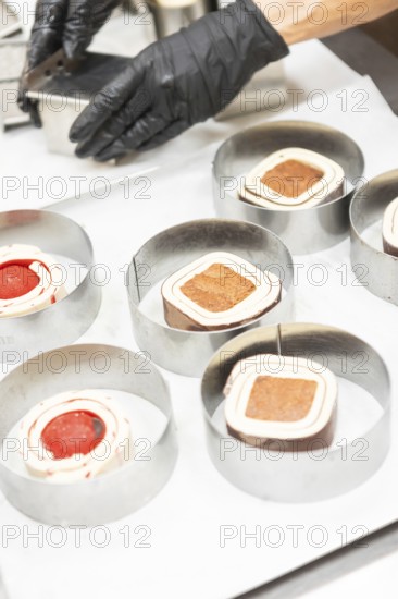 A close-up of a baker's hands wearing gloves, skillfully preparing Italian pastries in metal rings