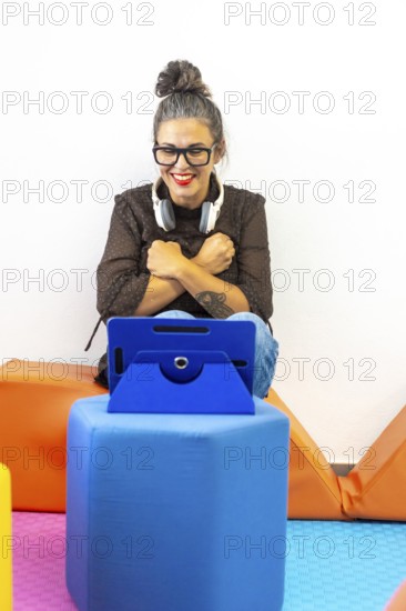 A woman teaching sign language through a video call, sitting on colorful cushions with a tablet