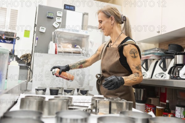 A skilled baker in an apron sprays molds for pastry preparation in a professional kitchen setting