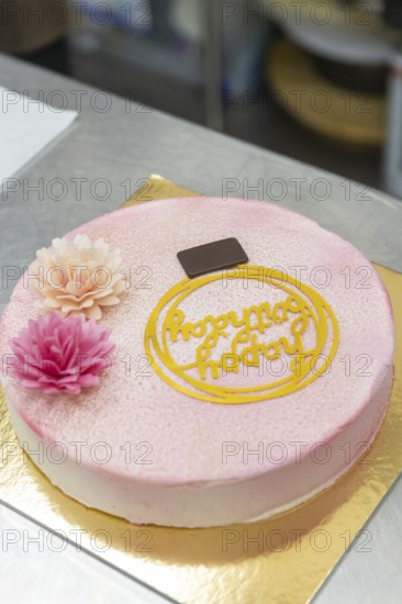 A beautifully decorated Italian cake with pink floral accents, a chocolate square, and an ornate