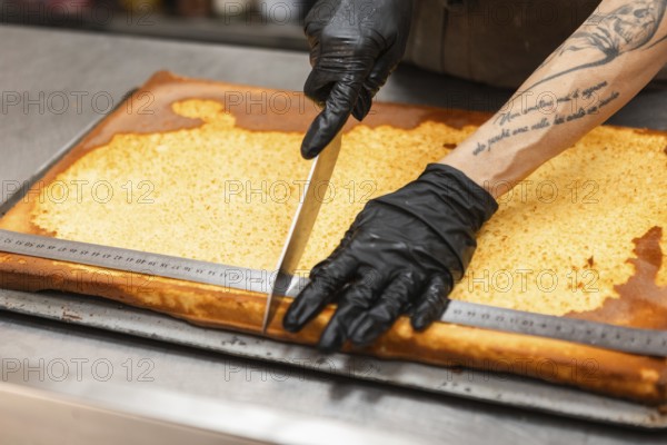 An artisan wearing gloves skillfully slices a traditional Italian cake with a large knife The large
