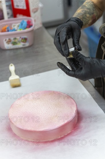 A skilled baker wearing gloves applies pink icing and gold dust to a cake in an Italian bakery The