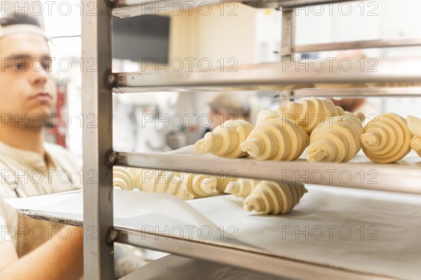 A baker carefully places freshly rolled croissants on a rack in a bustling Italian bakery The dough