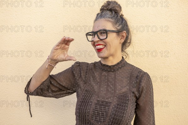 A woman with glasses and red lipstick enthusiastically demonstrates a sign language gesture