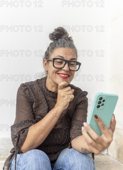 A woman with glasses uses a smartphone for a video call, focusing on learning sign language She is