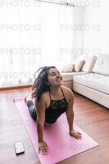 A young latin woman performs yoga on a pink mat in her cozy living room, enjoying a peaceful moment