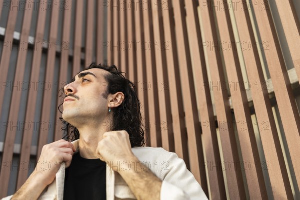 A man gazes upward with confidence, adjusting his collar against a modern architectural backdrop