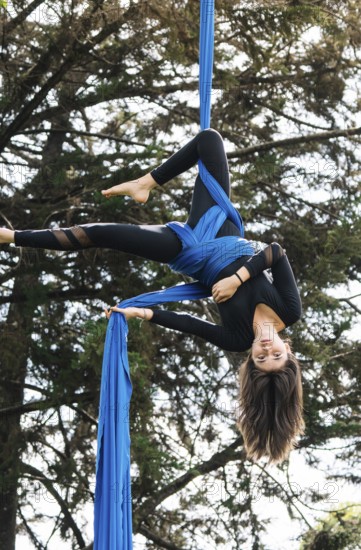 A skilled aerial performer demonstrates acrobatics on vibrant blue fabric in a tranquil Bogota