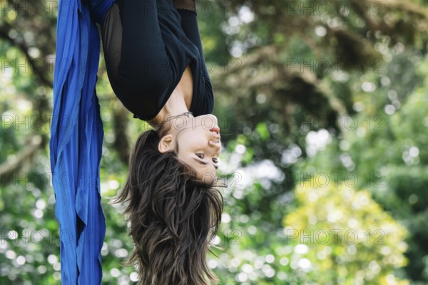Aerial acrobat performs elegant moves on blue fabric amidst lush greenery in a Bogota park The