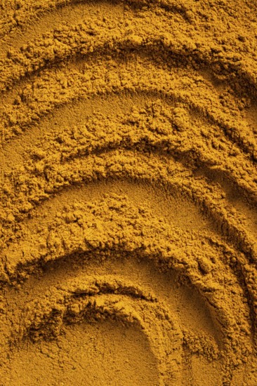 A vibrant close-up of golden curry powder, showcasing its textured surface with swirling patterns
