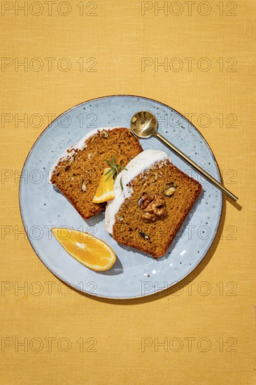Slices of carrot cake loaf topped with cream cheese frosting, garnished with walnuts, rosemary, and