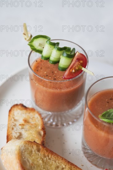 A refreshing glass of gazpacho garnished with cucumber, tomato, and bell pepper on a skewer Served