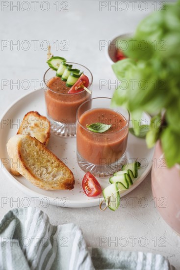 Two glasses of fresh gazpacho garnished with cucumber and tomato skewers, served with toasted bread