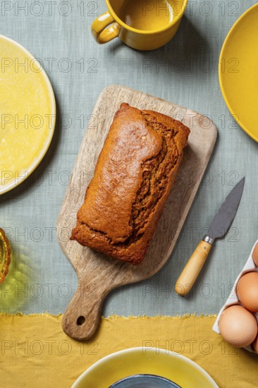 A freshly baked carrot cake loaf sits on a wooden board surrounded by a warm, autumn-themed table