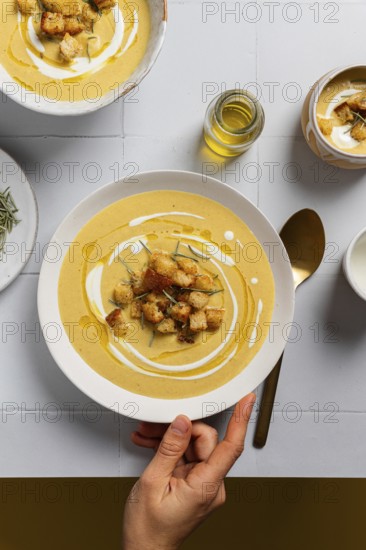 A creamy cauliflower curry soup garnished with croutons, rosemary, and drizzles of cream, served in