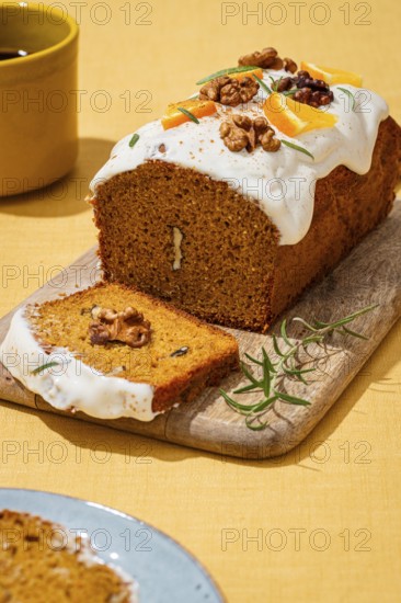 A freshly baked carrot cake loaf adorned with smooth cream cheese frosting, walnut pieces, and