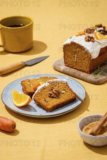 A tasty carrot cake loaf topped with creamy frosting and walnuts, presented on a yellow linen