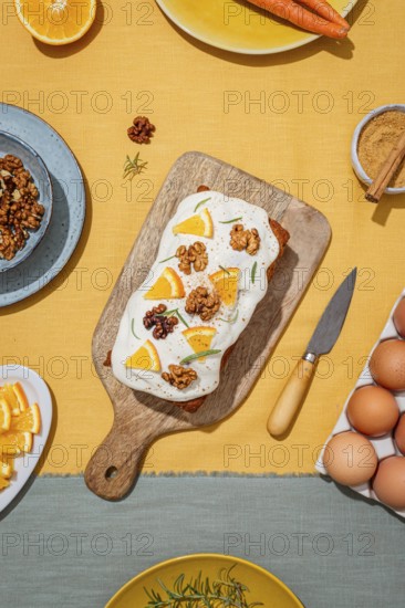 Carrot cake loaf topped with cream cheese frosting, orange slices, walnut, and rosemary Set on a