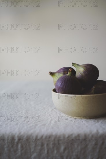 A close-up of fresh figs in a rustic bowl on a textured white tablecloth, creating a serene and