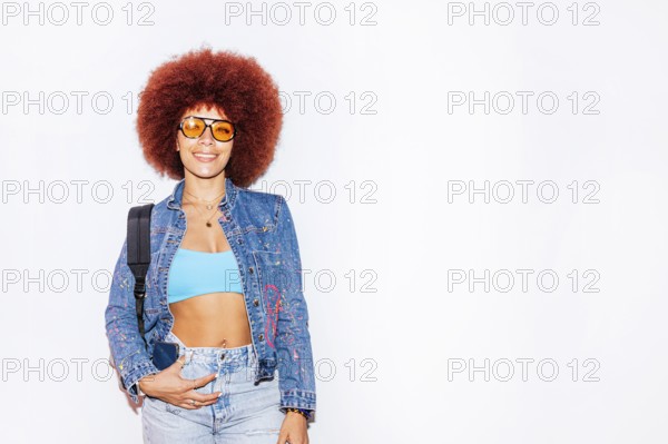 African descendant woman with a vibrant afro hair, smiling while wearing orange sunglasses and a
