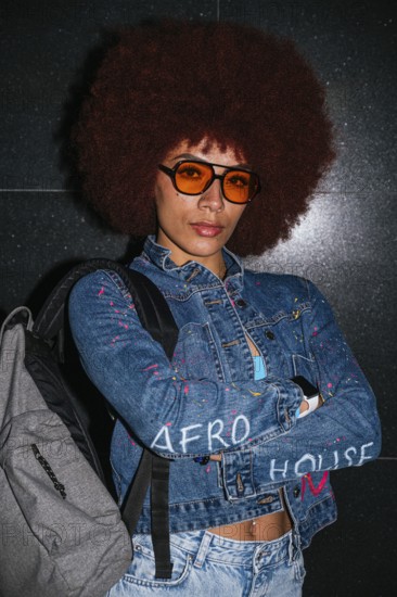 African descent woman with a voluminous afro hairstyle wearing orange sunglasses and a denim