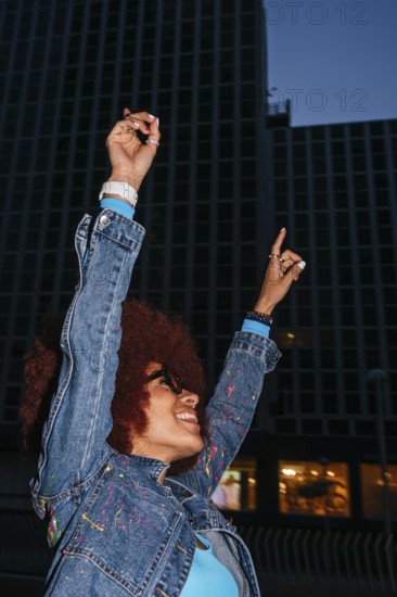 A joyful African descendant woman with afro hair raises her arms in celebration against a backdrop