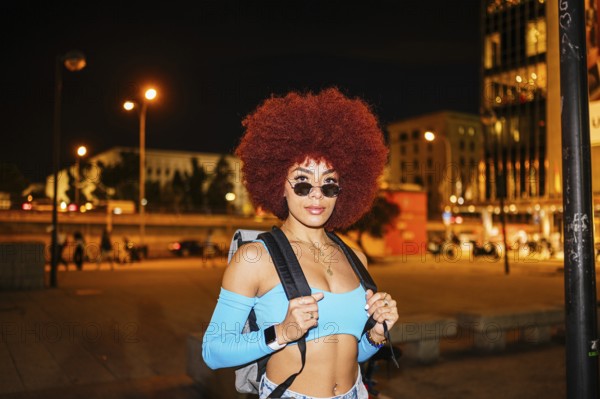 An African descendent woman with vibrant afro hair stands confidently on a city street at night.