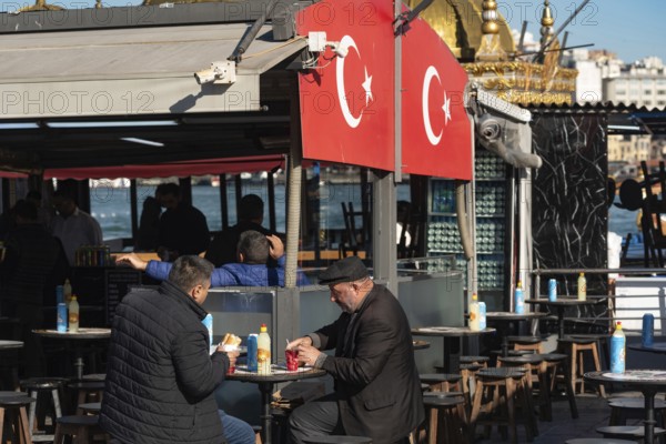 Istanbul, Turkey. November 21st 2023 Two Turkish men eat Balik Ekmek, a fish sandwich, a popular