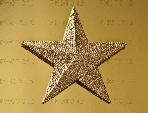 A golden Christmas star shines with a glittery surface against a textured golden background,