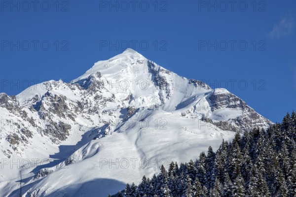 A stunning snow-covered mountain peak stands majestically against a backdrop of a clear, deep blue