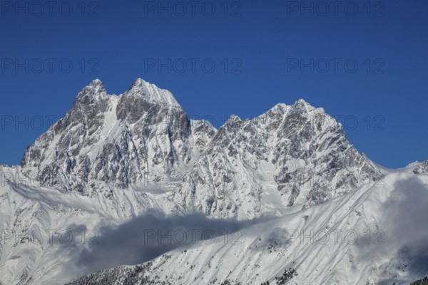 Majestic snow-covered mountain peaks tower under a clear blue sky, creating a breathtaking natural