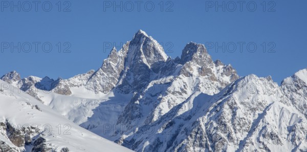 Majestic snow-covered mountain peaks rise against a clear blue sky, capturing the breathtaking