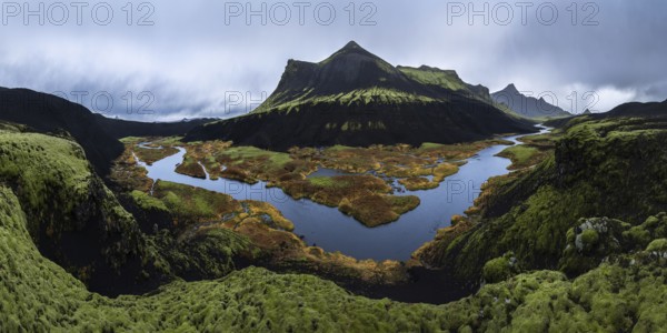 A stunning panoramic view of a moss-covered volcanic mountain with a winding river and colorful