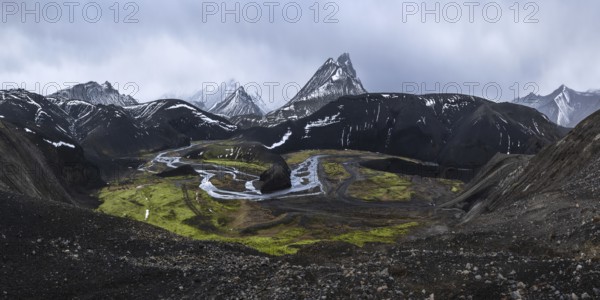 A striking view of black volcanic mountains partially covered in snow, with a winding river and