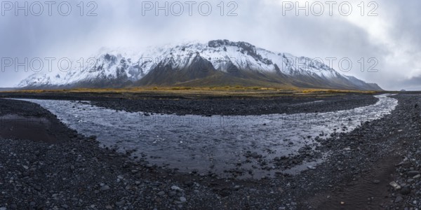 A dramatic view of a snow-covered mountain rising over a rocky riverbed in the Icelandic Highlands,